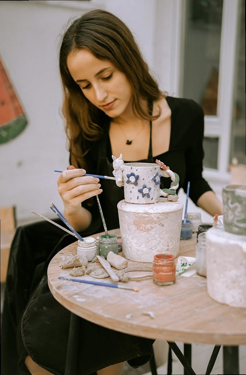 Une femme artiste peignant de la poterie en céramique avec des pinceaux et des peintures en plein air.